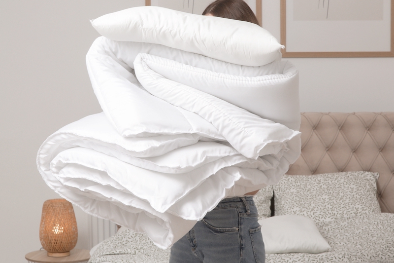 Bedding storage. Image shows a woman holding a pile of soft white folded bedding ready for storage.
