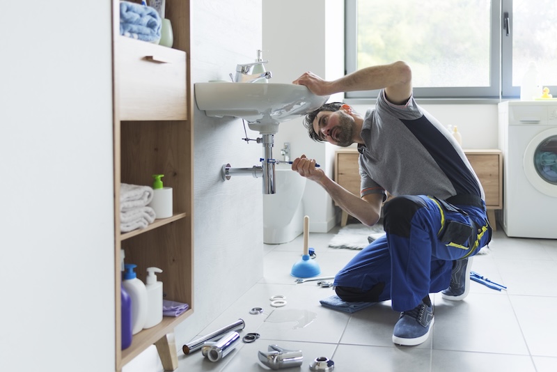 5 benefits of self storage for plumbers. Image shows a man inspecting underneath a sink. 