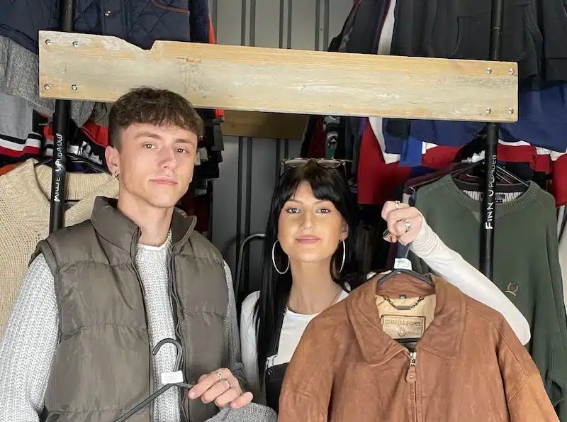The vintage rack case study. Image shows the couple behind the company in their storage unit, holding a few items of clothing.